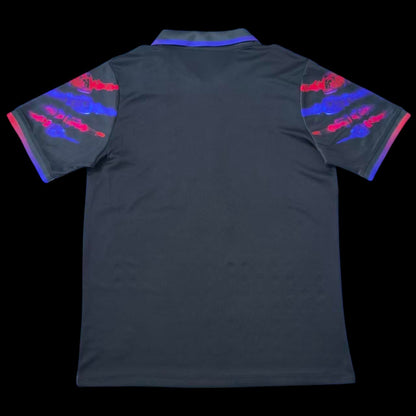 Maillot de football FC Barcelone noir avec col polo, manches noires ornées d'éclaboussures rouges et bleu-violet. Logo du club et Swoosh Nike.