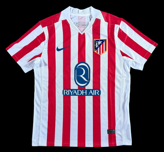 Maillot de football domicile Atletico Madrid homme rouge et blanc rayé, avec logo club et sponsor Riyadh Air. Tissu respirant.