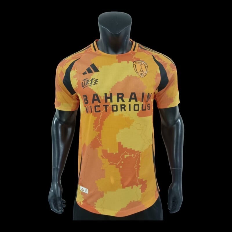 Maillot de football Paris FC Bahrain Victorious orange et jaune camouflage numérique, col rond, manches courtes, tissu respirant, logo équipe et sponsor.