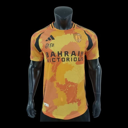 Maillot de football Paris FC Bahrain Victorious orange et jaune camouflage numérique, col rond, manches courtes, tissu respirant, logo équipe et sponsor.