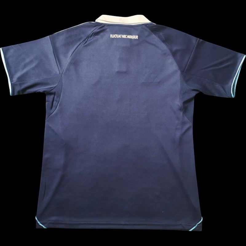 Maillot de football bleu marine pour homme Paris FC avec col polo blanc et détails bleu clair. Inscription "FLUCTUAT NEC MERGIUR" au dos.